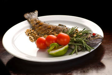 grilled fish served with tomatoes and herbs on white plate. 