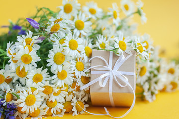 Chamomile flowers and gift or present box on yellow background. Holiday celebration concept.