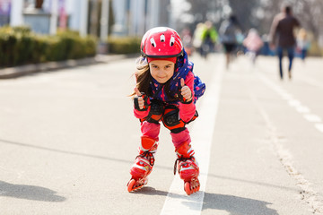 Funny Little pretty girl on roller skates in helmet riding in a park. Healthy lifestyle concept