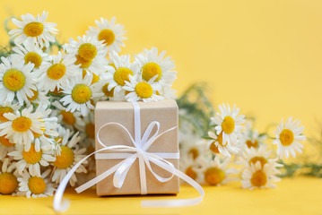 Chamomile flowers and gift or present box on yellow background. Holiday celebration concept.