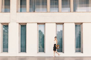 Fashionable tall business woman in sunglasses walking near a building with tall windows in the city
