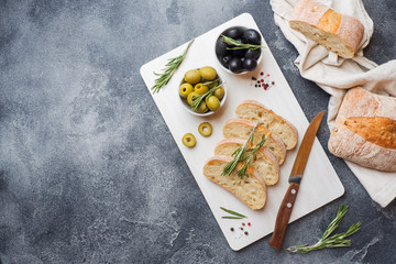 Italian ciabatta bread with olives and rosemary on a cutting Board. Dark concrete background. Copy...
