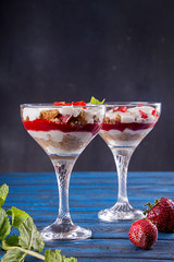 Summer cake in glass, strawberry sweet cherry layered trifle with biscuit, mascarpone and whipped cream on blue background