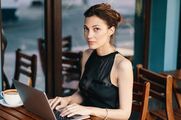 Refined business woman in glasses, sitting at table in cafe working at laptop