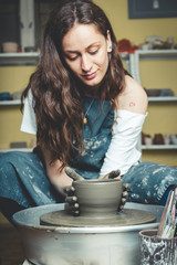 Smiling artisan woman working on pottery wheel and making a pot.