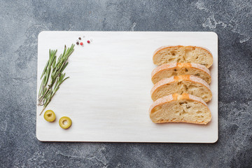 Italian ciabatta bread with olives and rosemary on a cutting Board. Dark concrete background. Copy...