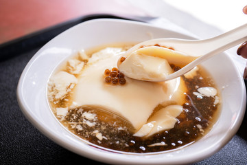 Popular Taiwan gourmet - Dessert of tapioca pearl ball (bubble) mixed bean curd tofu pudding (douhua, dou hua) in white bowl, close up, lifestyle