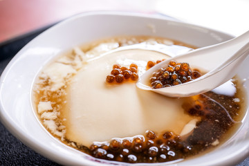 Popular Taiwan gourmet - Dessert of tapioca pearl ball (bubble) mixed bean curd tofu pudding (douhua, dou hua) in white bowl, close up, lifestyle