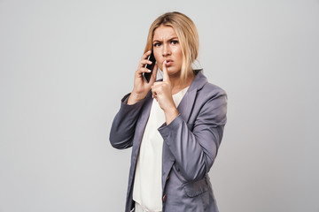 Serious young pretty woman posing isolated over grey wall background talking mobile phone.