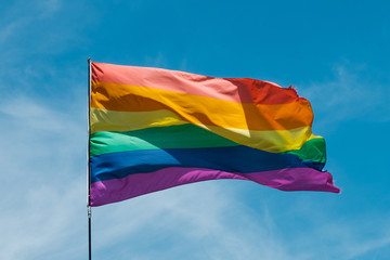 Gay rainbow flag waving with blue sky background - symbol of Gay Pride  -