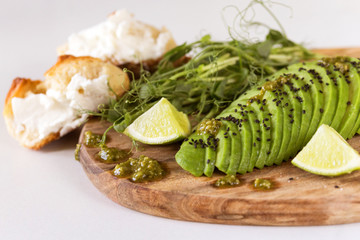 Breakfast with avocado, bun, pea sprouts, lime, pesto and coffee.