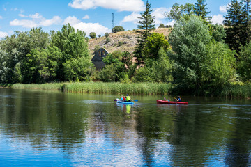 Beautiful landscape of a river in the middle of nature, a beautiful blue sky with clouds and far away people walking in kayak by the river.