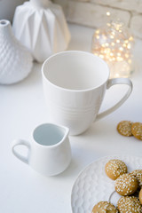 Simple white mug and a creamer on white table with cookies