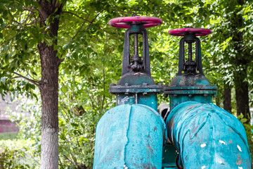 two turquoise blue rusty old pipes with red vents against a background of forest trees; environmental pollution concept