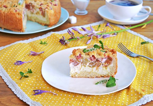 Dessert, sliced shortcrust cake with rhubarb and cottage cheese or ricotta on a white plate.