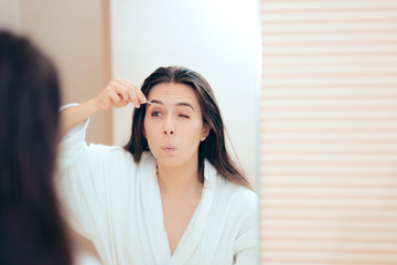 Fototapeta premium Woman Wearing Bathrobe Plucking her Eyebrows After Shower