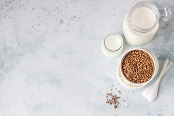Buckwheat and rice in white bowls and milk jug. Healthy breakfast. Light stone background. Copy space.