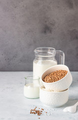 Buckwheat and rice in white bowls and milk jug. Healthy breakfast. Light stone background. Copy space.