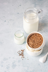 Buckwheat and rice in white bowls and milk jug. Healthy breakfast. Light stone background. Copy space.