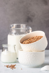 Buckwheat and rice in white bowls and milk jug. Healthy breakfast. Light stone background. Copy space.