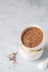 Buckwheat and rice in white bowls. Healthy breakfast. Light stone background. Copy space.