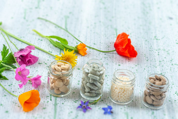 Herbal supplements and vitamins on wooden tray , decorated with colorfull medicinal flowers and herbs blurry wooden background
