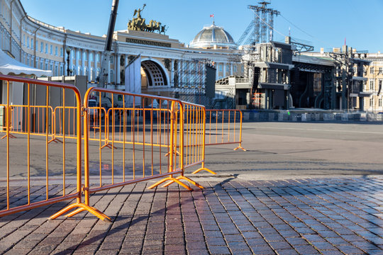 metal barriers to limit entry. Yellow metal fence to protect the passage to the Palace Square in St. Petersburg. In the background is the Arc de Triomphe and a stage for performances.  - Powered by Adobe
