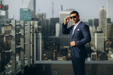 A handsome man wearing glasses in a classic suit wears a background of modern buildings