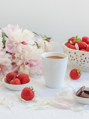 Coffee cup with chocolate, strawberries and peonies in the background