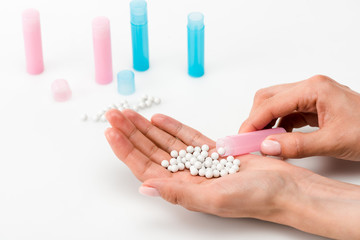 cropped view of woman holding round pills in hand near blue and pink bottles on white