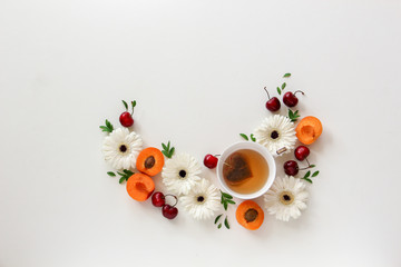 Flatlay composition of flowers and fruits with a cup of tea with heart shape tea bag on a bright background. Copy space
