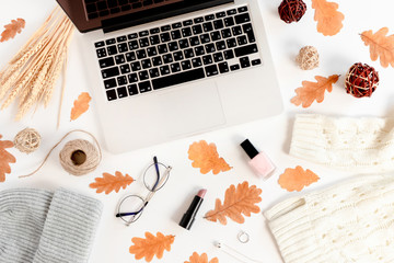 White desk with laptop, dry leaves, women's cosmetics, clothes and accessories