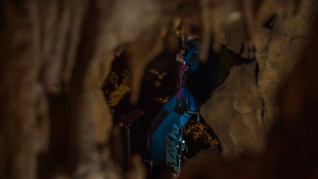 A climber is slowly going down on a rope. He is exploring the caves.