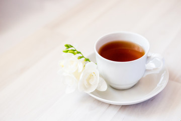 cup of tea on a saucer and a white freesia flower