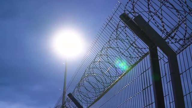Large military fence with barbed wire at night lit by a lantern. Secret military base