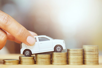 close up hand holding model of toy car white on over a lot money of stacked coins - insurance, loan...