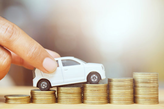 close up hand holding model of toy car white on over a lot money of stacked coins - insurance, loan and buying car finance concept. buy and installments down payment a car
