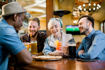 Group of five multiethnical friends having pizza at cafe. Cheerful young people eating pizza, drinking cocktails and enjoying at a fast food restaurant.