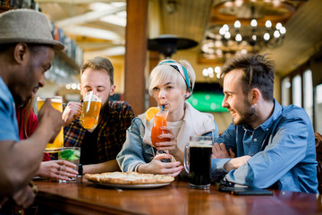 Group of five multiethnical friends having pizza at cafe. Cheerful young people eating pizza, drinking cocktails and enjoying at a fast food restaurant.