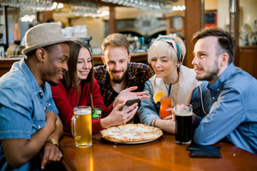 Group of young cheerful friends are sitting in a cafe, eating, drinking drinks. Friends take selfies and take pictures.