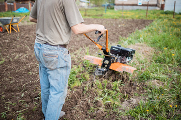 Agricultural machinery: cultivator for tillage in the garden. man Farmer plows the land with a cultivator, preparing it for planting vegetables, in a sunny garden.