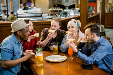 Cheerful multiracial friends having fun eating pizza in pizzeria.