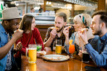 Five cheerful young multiethnical friends sharing pizza in a indoor cafe