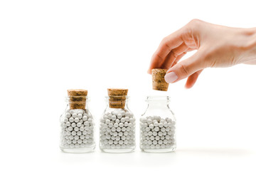 cropped view of woman touching wooden cork near glass bottles with pills isolated on white