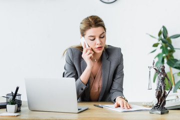 beautiful lawyer sitting in office, looking at document and talking on smartphone