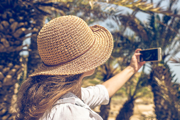 Fototapeta premium Woman in the straw hat taking selfie picture or video using smartphone in the palm forest. Seychelles islands