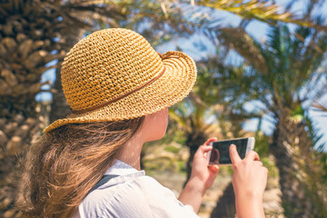 Woman in the straw hat taking selfie picture or video using smartphone in the palm forest. Seychelles islands