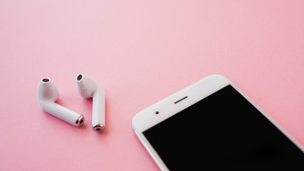 White wireless headphones and smartphone are lying on a bright pink background. Headphones out of...