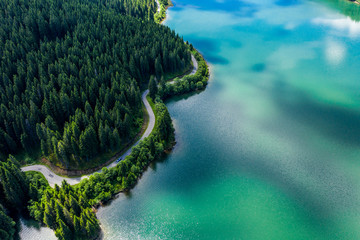 Aerial view over beautiful turquoise mountain lake and green forest. Spring in the mountains. Green forest, mountain lake. Green pine and fir trees forest and a lake. Beautiful mountain road. - Image