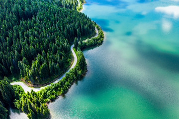 Aerial view over beautiful turquoise mountain lake and green forest. Spring in the mountains. Green forest, mountain lake. Green pine and fir trees forest and a lake. Beautiful mountain road. - Image